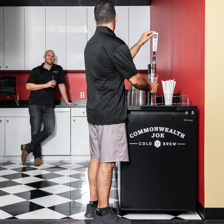 Two coworkers enjoying Commonwealth Joe nitro cold brew coffee in a bold, modern breakroom — highlighting the energy and appeal of premium office beverage service.