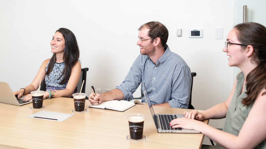Happy and engaged office employees collaborating in a meeting room with laptops and Commonwealth Joe cold brew coffee on the table — showcasing premium office coffee service.
